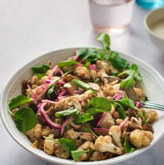 Roasted cauliflower with spices, watercress, pickled onions, and almonds in a white bowl.