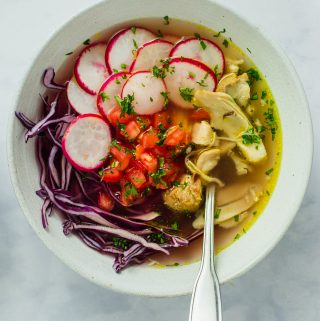 a white bowl filled with fresh cabbage, radishes, tomatoes, and poached chicken. topped with chicken broth