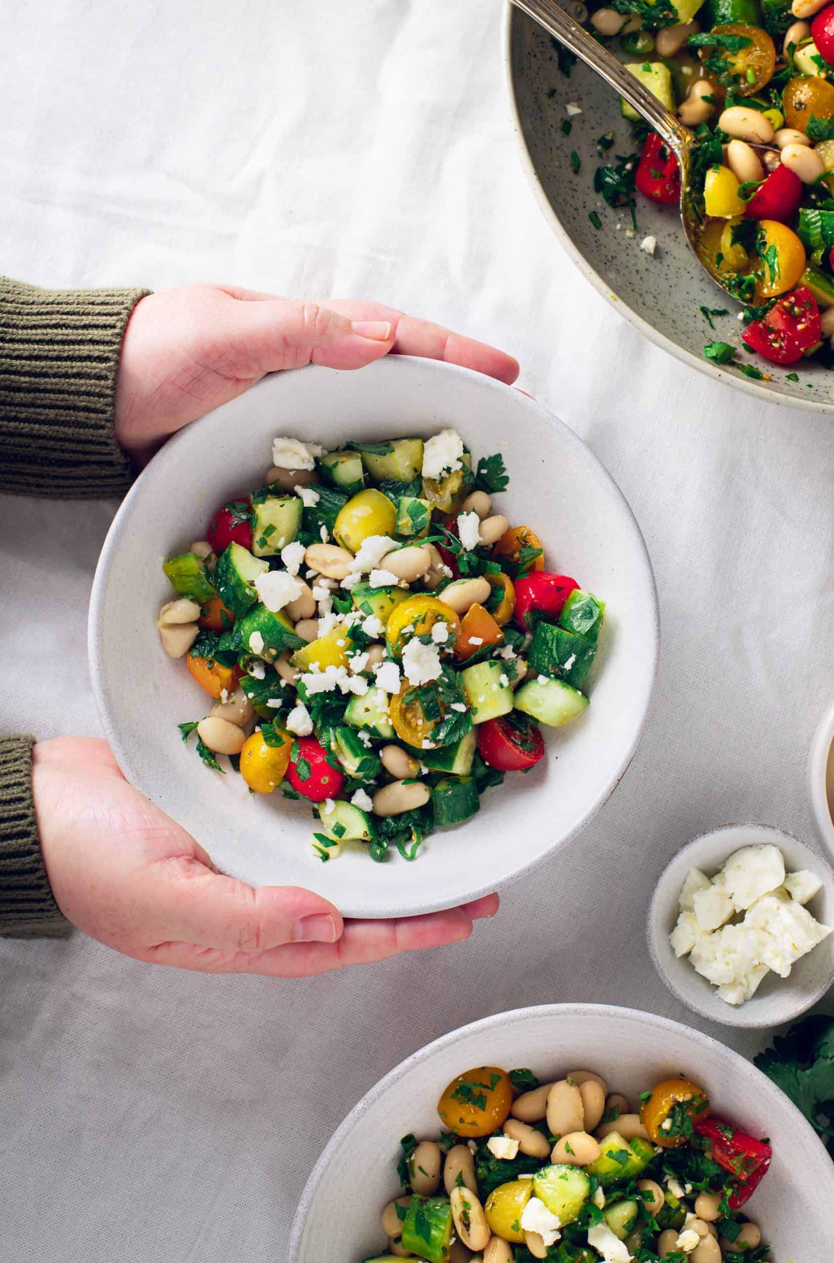 three bowls of simple bean salad: one bowl is being set on the table