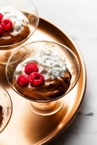 two glasses of avocado pudding with whip cream and raspberries on top