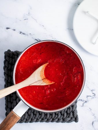 san marzano tomato sauce in a white pot on a dark grey hot pad and a white lid on the side