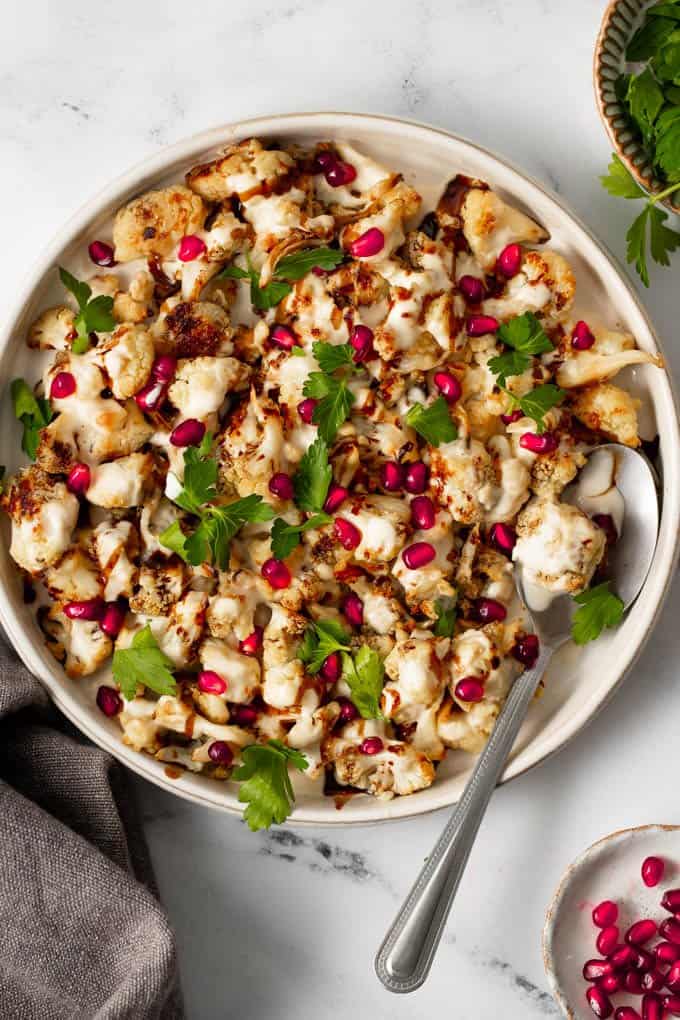 A white plate filled with roasted cauliflower tahini parsely and pomegranates 