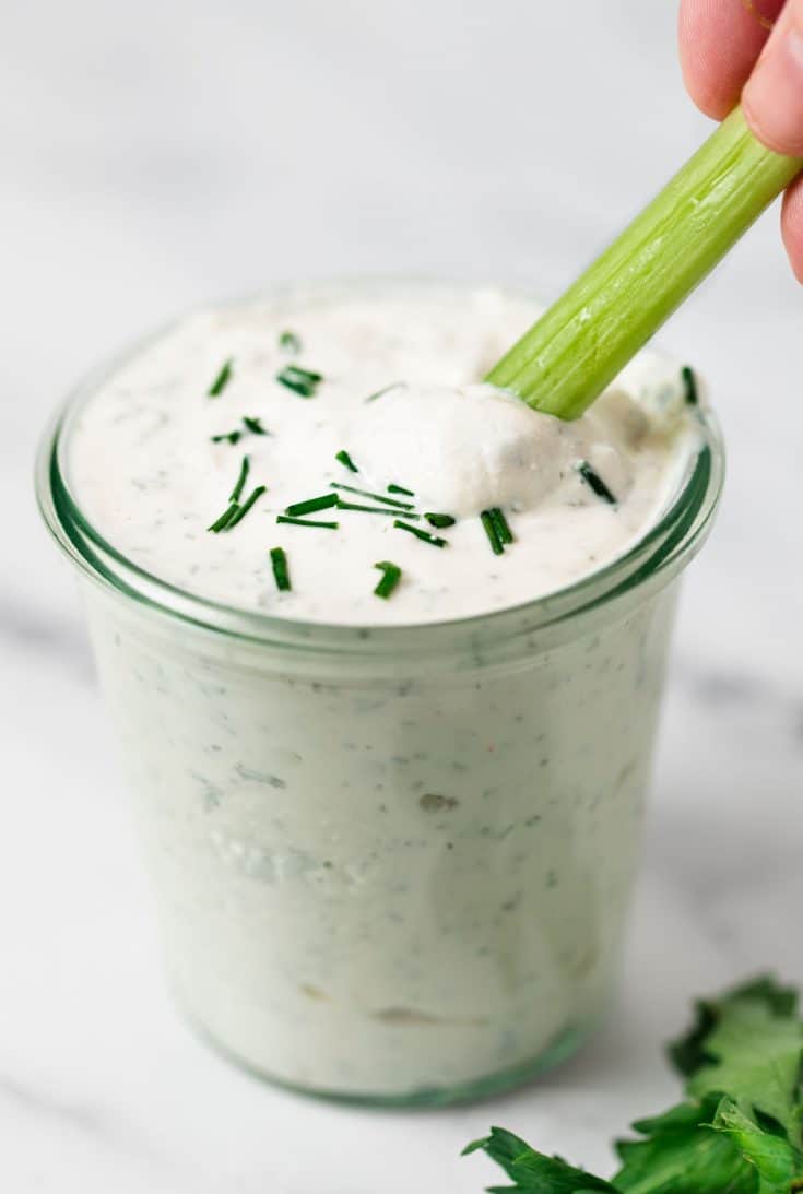 Healthy ranch dip in a jar being dipped with a piece of celery