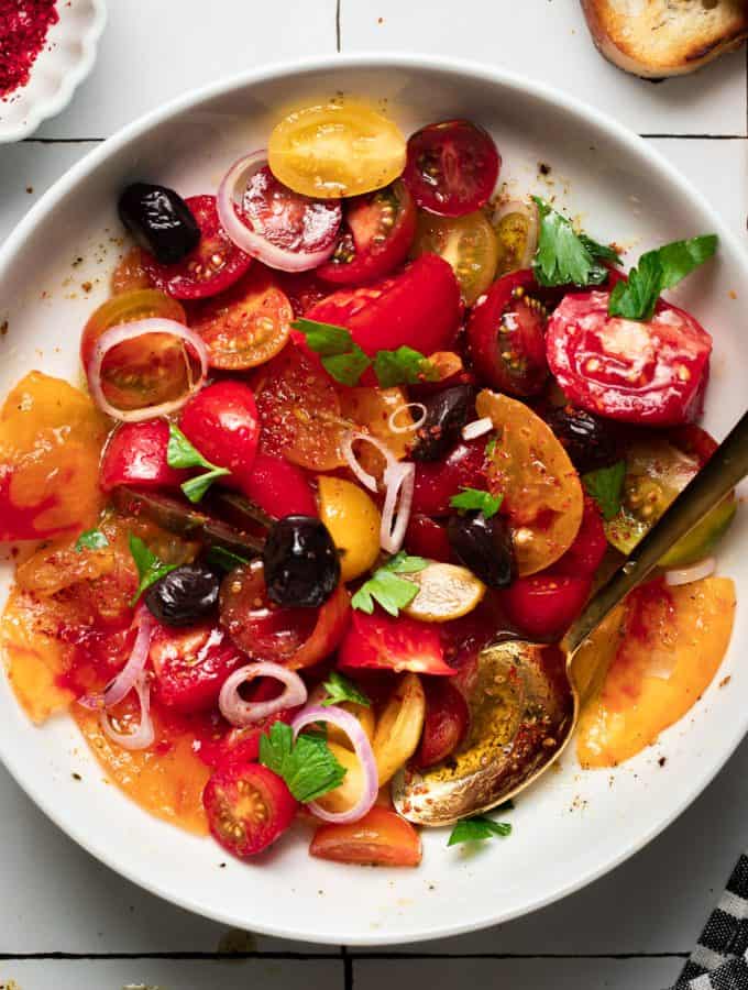 heirloom tomato salad in a white bowl and gold spoon
