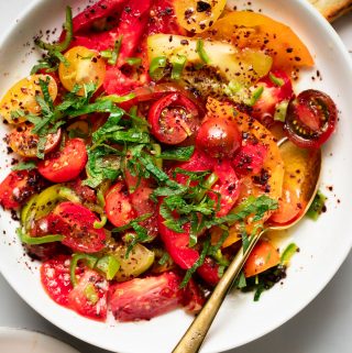 close up of tomato sumac salad in a white bowl with a gold spoon