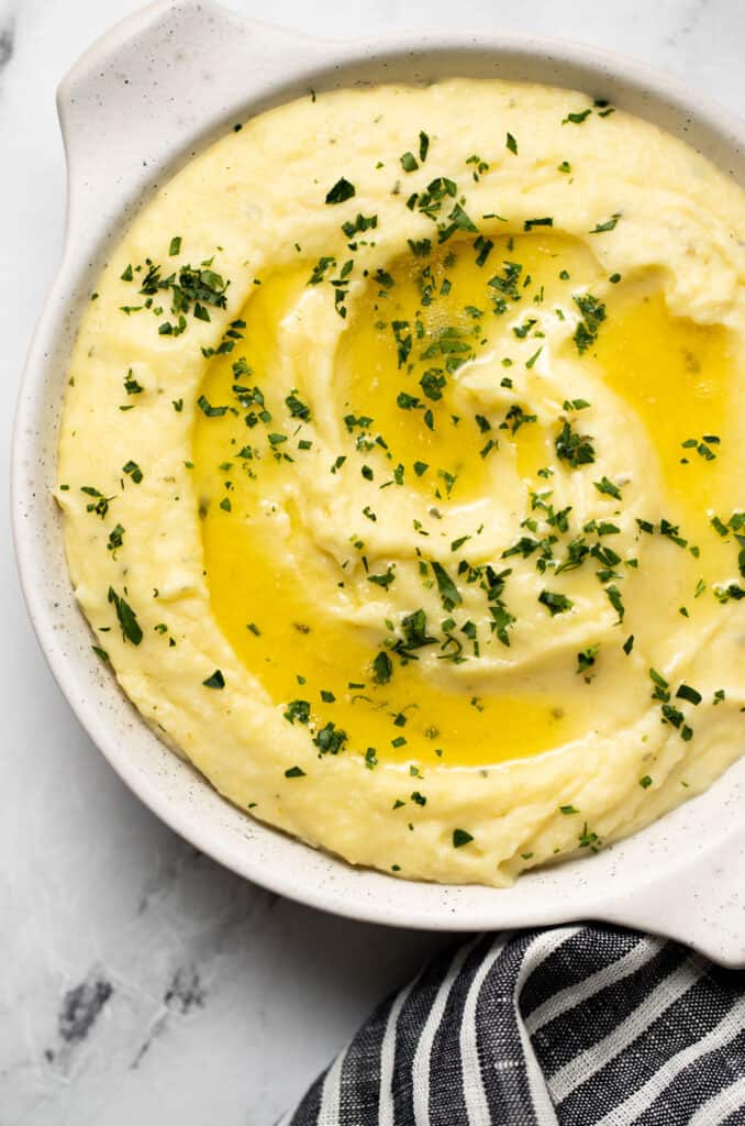 Boursin Mashed Potatoes in a white serving bowl topped with melted butter & parsely